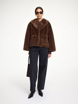 Woman wearing a brown faux fur coat that features a pointed collar, neck tie, and front pockets.
