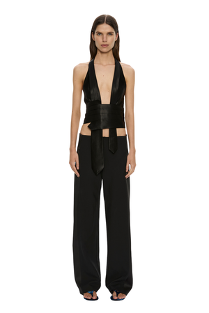 A model stands against a solid white background wearing a black halter-neck wrap top with a matching wide-leg pant set.