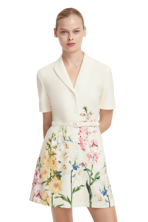 A model wearing a short-sleeve cream-colored blazer-style top with a matching belt and a flared skirt featuring a colorful floral print.