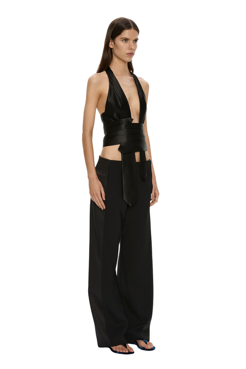 A model wearing a black halter crop top with a wide waist tie and matching black wide-leg trousers, standing against a plain white background.