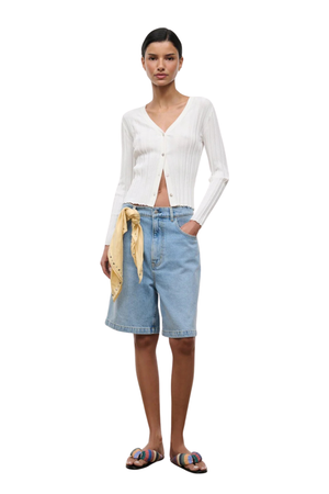 A woman wearing a white long sleeve button cardigan with blue denim shorts