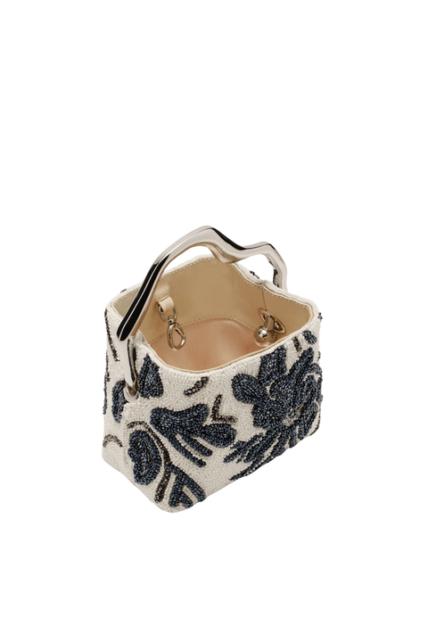 A small structured handbag with a cream canvas body, black beaded floral pattern, and a silver-tone metal top handle, shown on a plain white background.