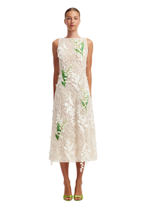 A model wearing a sleeveless cream lace midi dress with green floral applique, paired with lime green high-heeled sandals, against a plain white background.