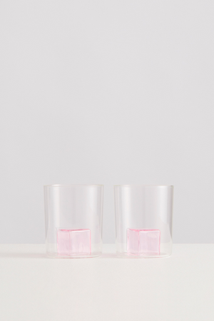 Two clear glasses with pink glass ice cubes inside on a white background