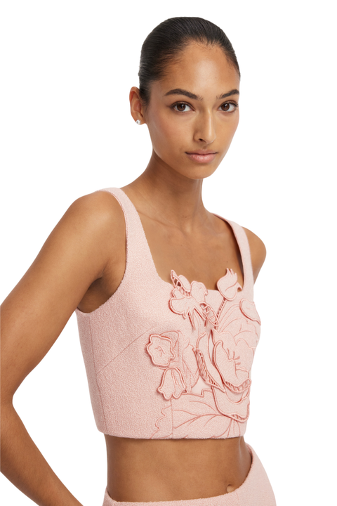 A model wearing a light pink textured crop top with 3D floral applique, photographed against a solid white background.