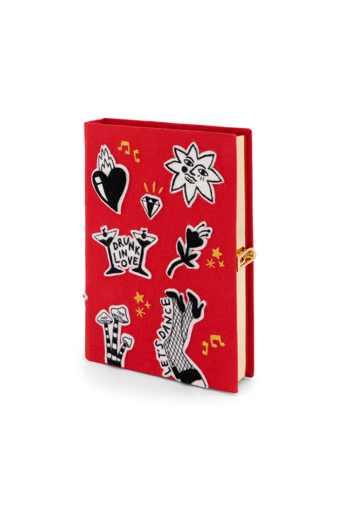 A red book clutch featuring a collage of black and white graphic stickers and small yellow musical notes, shown on a clean white background.