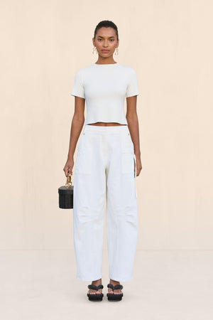Woman wearing a white knit short sleeve t-shirt, paired with white barrel leg pants and black sandals.