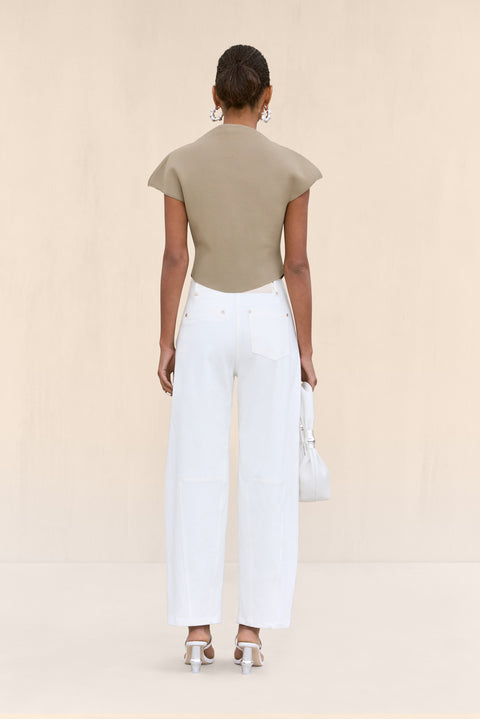 back-facing woman wearing a tan knit shirt that features a mock neck and structures cap sleeves, paired with white cargo pants.