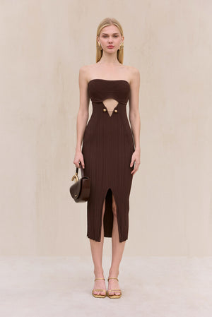 Woman wearing a brown knit, strapless midi dress with cut-out design at the bust featuring gold hardware, and a front slit, paired with gold shoes.