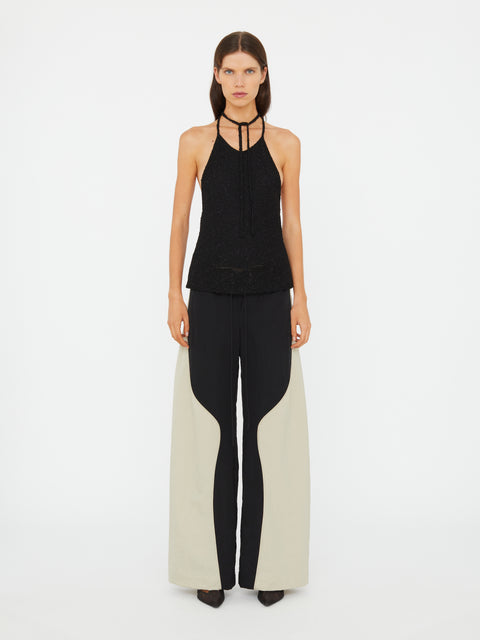 Woman wearing a black halter top and black and white pants on a white background