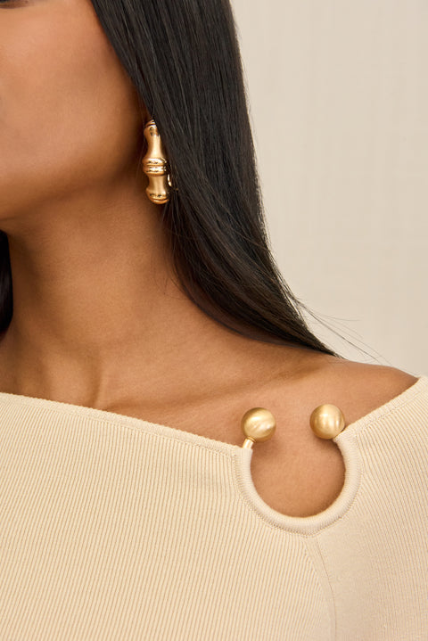 Detail shot of a woman wearing a cream long sleeve shirt with a ring detail at the shoulder.