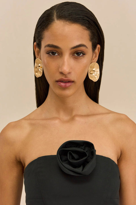 Pair of gold oversized earrings on a model wearing a black strapless top.