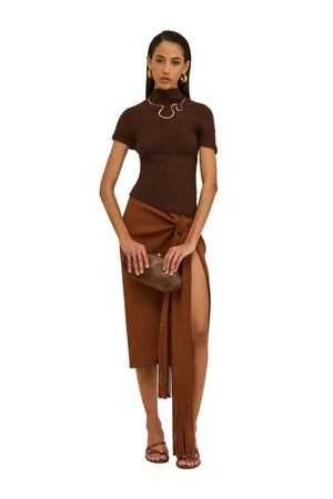 Woman wearing a brown ribbed top and skirt with a clutch on a beige background