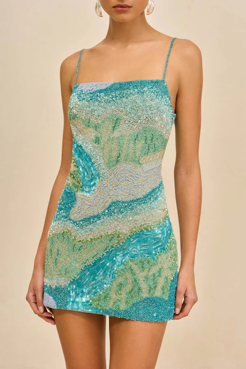 Detail shot of woman wearing a blue, green, and beige patterned dress on a beige background
