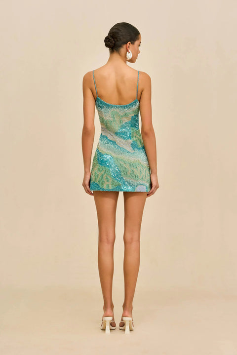 Back view of woman wearing a blue, green, and beige patterned dress on a beige background.