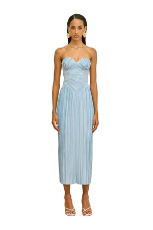 Woman wearing a light blue strapless pleated dress against a beige background.