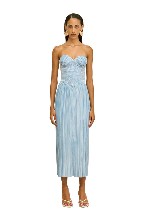 Woman wearing a light blue strapless pleated dress against a beige background.