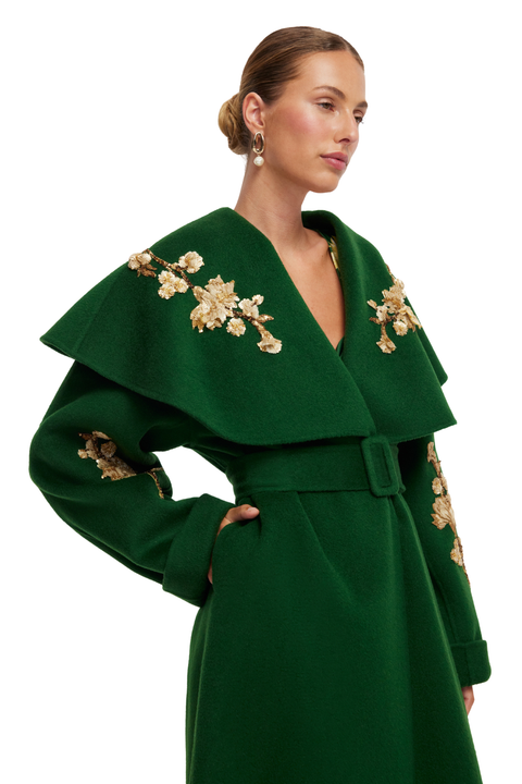 Green coat with floral embellishments worn by a model on a white background