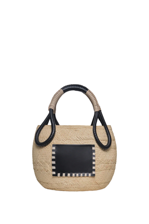 A woven straw handbag with a black rectangular front patch bordered in white, featuring two twisted rope handles with black trim, shown against a plain white background.