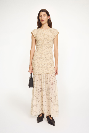 Woman wearing a bodycon patterned dress holding a black handbag on a white background