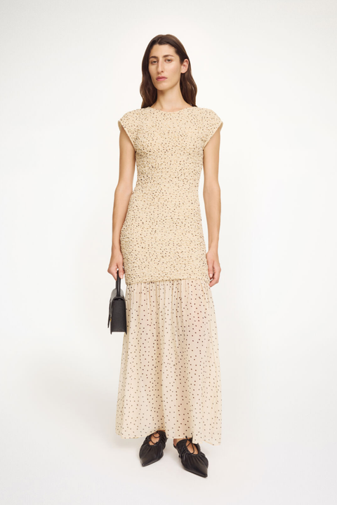 Woman wearing a bodycon patterned dress holding a black handbag on a white background