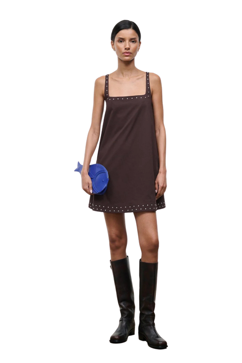 Woman wearing a brown sleeveless square neck mini dress with studs on a white background with a cobalt blue fish bag