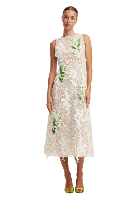 A model wearing a sleeveless, knee-length cream lace dress with green floral embroidery, paired with lime green high-heeled sandals, against a plain white background.