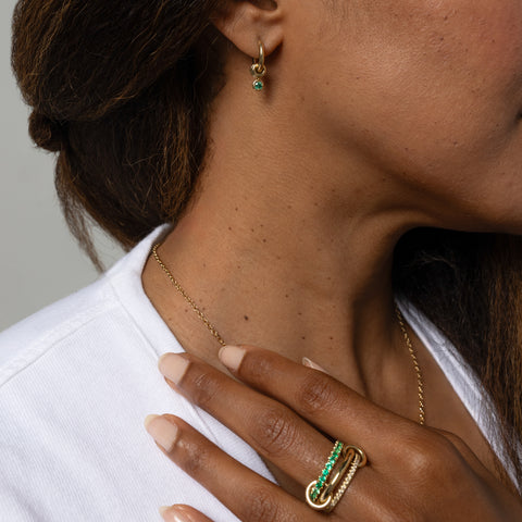 A woman wearing a Spinelli Kilcollin Norah ring that features a 1.7mm yellow gold band pave with diamonds, a 2.3mm yellow gold band, and a 2.8mm yellow gold band pave with emeralds, connected by two yellow gold connectors.