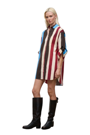 A blonde model wearing a colorful striped shirt dress with vertical red, brown, cream, and blue stripes, styled with black knee-high leather boots against a plain white background.