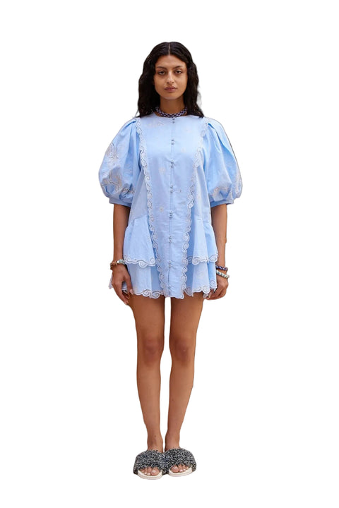 Woman wearing a light blue dress with lace detailing against a white background.