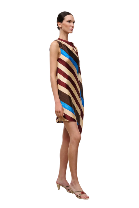 A woman modeling a sleeveless, knee-length dress with diagonal stripes in beige, brown, burgundy, and bright blue, paired with beige heeled sandals, set against a plain white background.