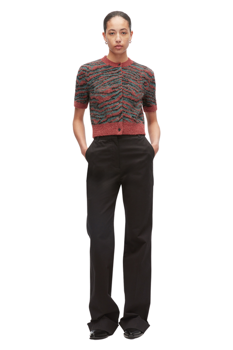 A model stands against a white background wearing a short-sleeve knit cardigan with a red, green, and black tiger print pattern, paired with black wide-leg trousers.