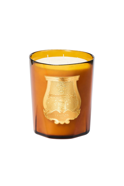 An amber murano glass jar candle with a gold crest emblem on the front, set against a plain white background.