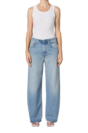 Person wearing light blue mid-rise jeans and a white tank top on a white background facing forward