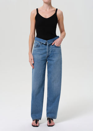 Woman wears blue jeans with fold over at waist and black tank top.