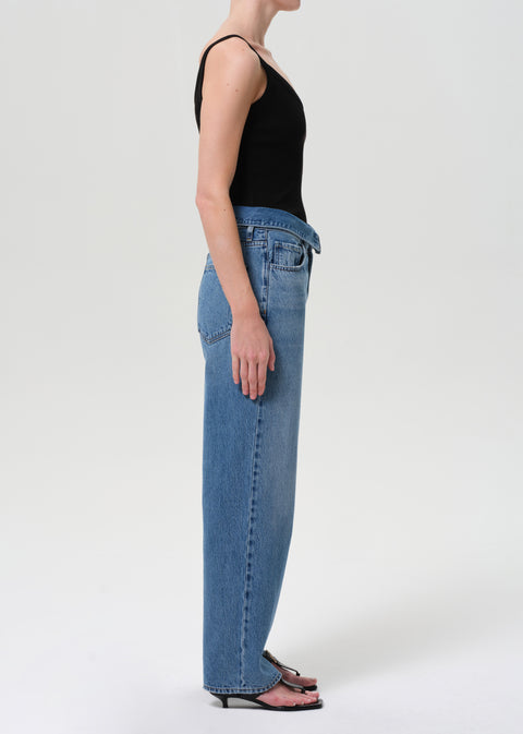 Side view of woman wearing blue jeans with fold over waist and black tank.
