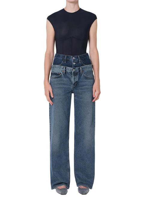 Person wearing a navy sleeveless top and blue two-toned, high-rise layered jeans on a white background from the front