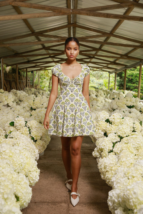 Model wears printed cotton mini dress on runway lined with white florals.
