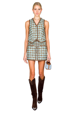 Woman wears blue and brown check vest and matching mini skirt adorned with rhinestones and brown tall boots.
