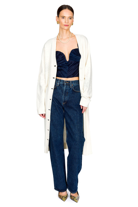 Woman wearing a white cardigan, navy top, and blue jeans on a white background