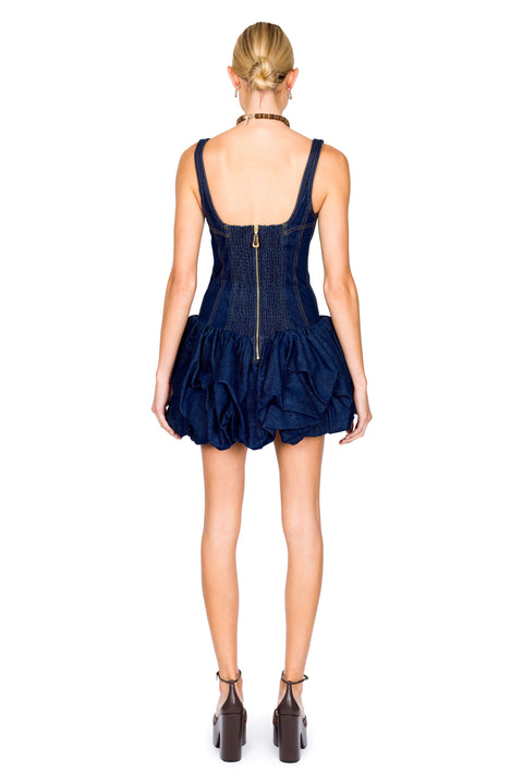 Woman wearing a navy blue denim mini dress with ruffled skirt on a white background from the back