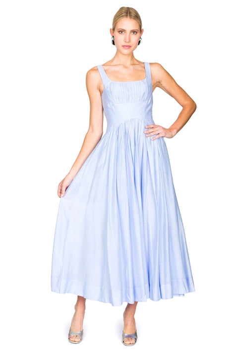 Woman holding skirt of a light blue maxi dress on a white background