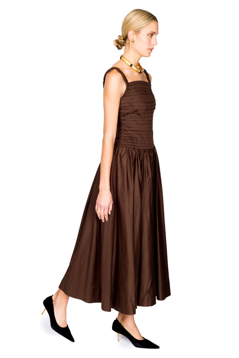 Woman walking to the right wearing a brown cotton maxi dress on a white background