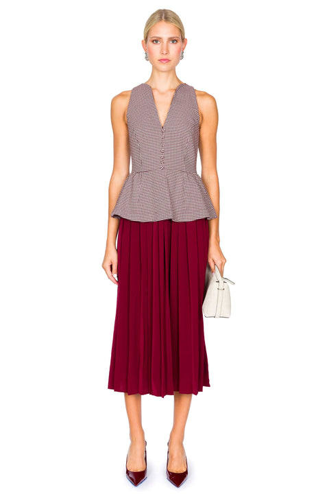 Woman wearing a sleeveless houndstooth patterned top and burgundy pleated skirt dress on a white background