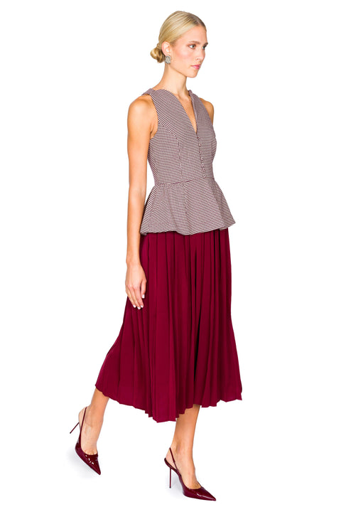 Woman walking to the right wearing a sleeveless houndstooth top and burgundy skirt midi dress on a white background