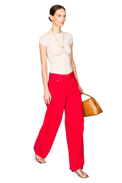 Woman taking a step to the right wearing red denim pants and sheer short sleeve baby tee holding a brown leather bag.