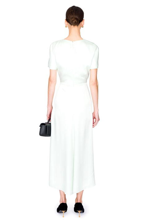 Woman facing away wearing a light green dress holding a black handbag on a white background