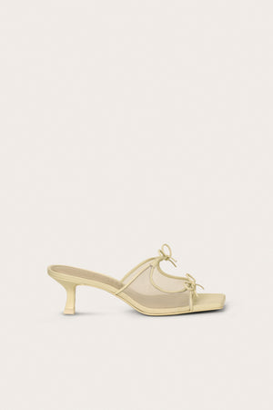 Side profile of a cream, open-toe kitten heal that features a mesh side panel design and two bows on the top of the foot.