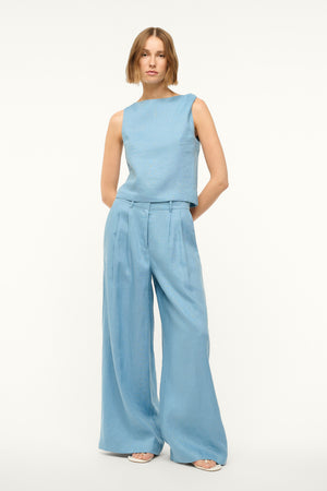Woman wearing a blue linen tank top with a twist detail in one shoulder, paired with matching trousers.
