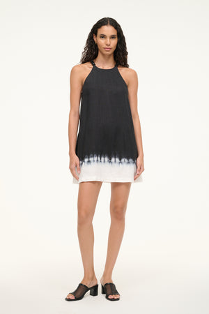 Woman wearing a black and white tie die, shift mini dress that features a beaded halter neck and a-line silhouette, paired with black sandals.